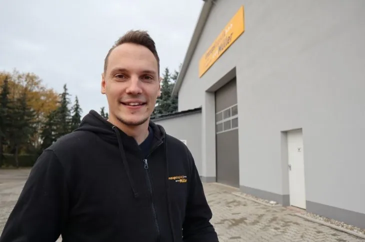 umzugshelfer laechelt vor firmengebaeude der umzugsfirma